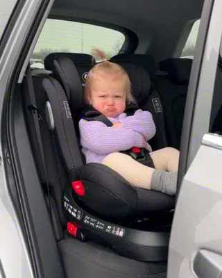 Toddler in a car seat wearing only a sweater, pouting